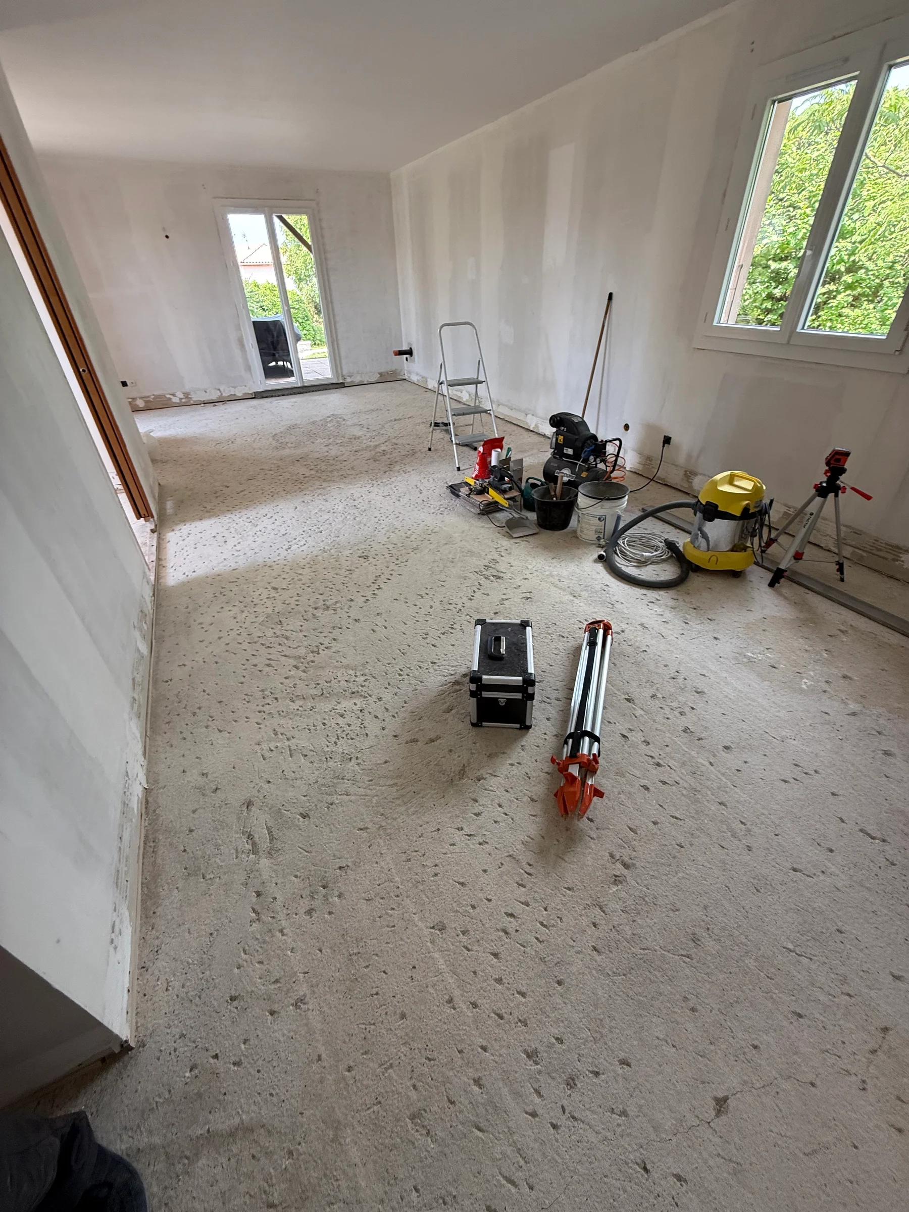 Séjour vidé de ses meubles pendant la rénovation, avec sol déposé, murs en préparation et outillage
